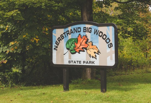 Sign for Nerstrand Big Woods State Park featuring colorful leaves and greenery in the background.