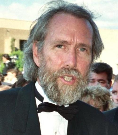 A man with a beard and long hair wearing a tuxedo and bow tie, smiling at an outdoor event.