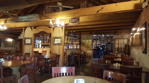 Cozy restaurant interior with wooden tables, chairs, and a rustic bar area, featuring exposed brick and beams.