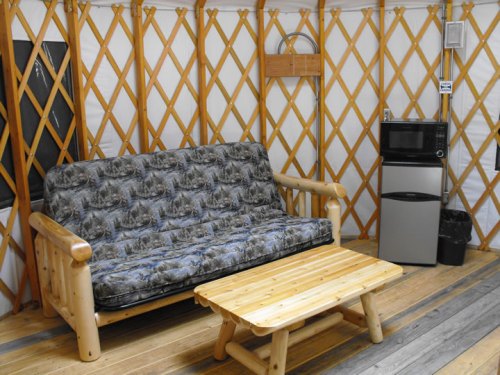 Interior of a yurt featuring a sofa, wooden coffee table, mini fridge, and wooden lattice walls.