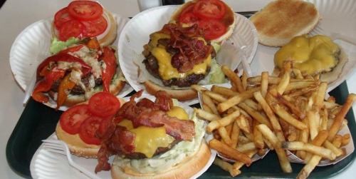 A tray with three burgers topped with cheese, bacon, and tomatoes, alongside a serving of crispy French fries.