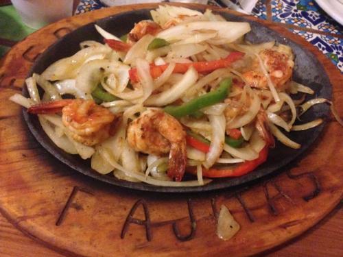 Sizzling shrimp fajitas with onions and bell peppers served on a wooden platter.