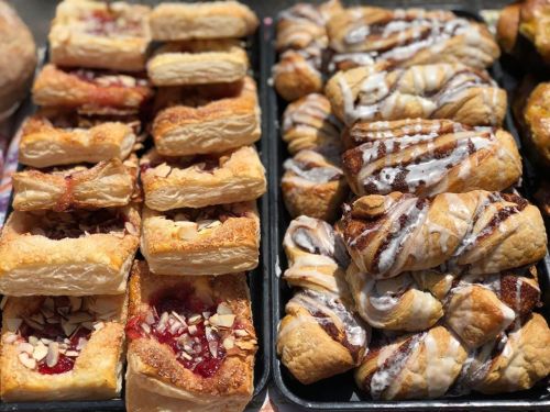 A variety of pastries, including fruit-filled squares and cinnamon rolls, displayed on trays.