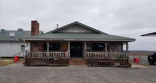 A rustic wooden building with a green metal roof, featuring a porch and various vintage signs.