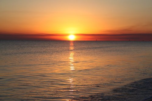 A serene sunset over calm waters, with vibrant orange and yellow hues reflecting on the surface.