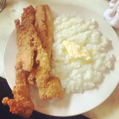 A plate with three pieces of fried fish and a serving of creamy grits topped with a pat of butter.