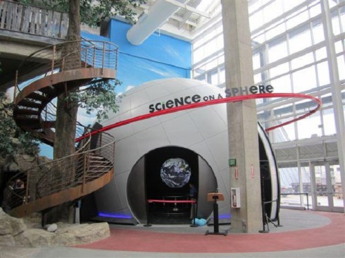 A spherical exhibit titled "Science on a Sphere" inside a modern building, featuring a spiral staircase and a globe display.