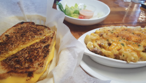 A grilled cheese sandwich with melted cheese beside a bowl of cheesy macaroni and a side salad.
