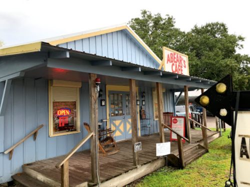 A blue café building with a sign reading "Abe's Café," featuring a porch and an "Open" neon sign.