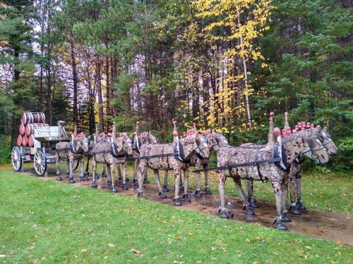 A whimsical sculpture of horses pulling a wagon, set in a forest with autumn foliage.