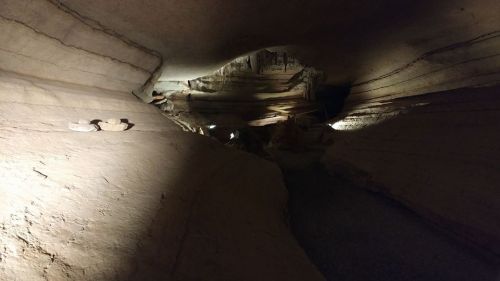 A dimly lit cave with layered rock formations and a winding path, illuminated by soft lights along the walls.