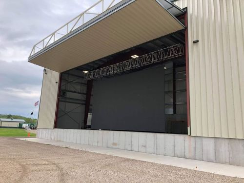 A large outdoor stage with a blank screen, set against a cloudy sky and surrounded by gravel.