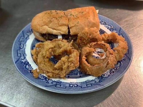 A plate with a split sandwich and crispy onion rings, garnished with herbs on a decorative blue and white plate.