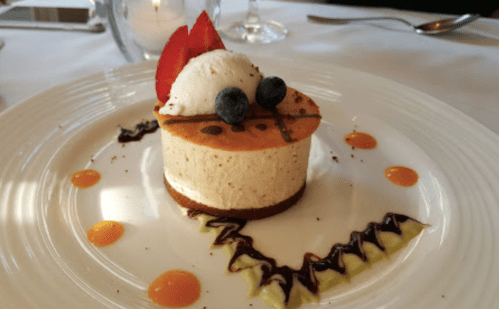 A dessert featuring a cheesecake topped with ice cream, strawberries, and blueberries, garnished with colorful sauces.