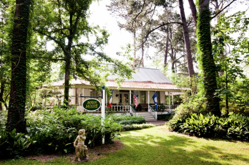A charming house surrounded by trees and greenery, featuring a porch and a sign that reads "Mckin House."