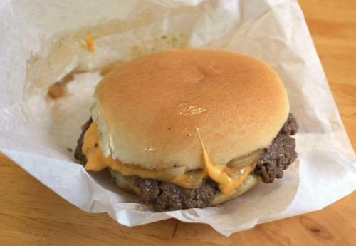A cheeseburger with melted cheese and a beef patty, served in a paper wrapper on a wooden surface.