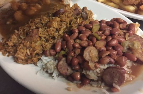 A plate of rice with sausage, red beans, and a side of gravy, showcasing a hearty, flavorful meal.