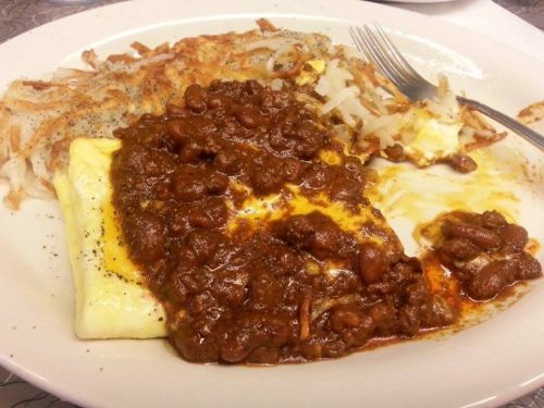 A plate of breakfast featuring an omelet topped with chili, served with hash browns and a fork on the side.