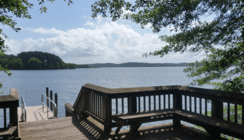 A serene lake view from a wooden dock, surrounded by trees and under a partly cloudy sky.