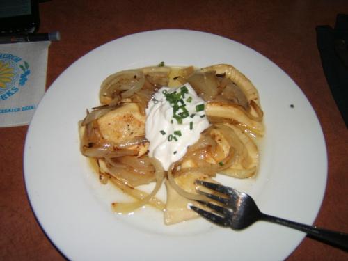 A plate of pierogi topped with sautéed onions, sour cream, and chives, served with a fork on the side.