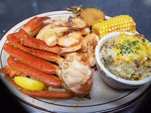 A seafood platter featuring crab legs, shrimp, a corn on the cob, a hushpuppy, and cheesy mashed potatoes.