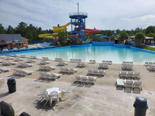 A large water park with empty lounge chairs, a wave pool, and colorful water slides in the background under a clear sky.