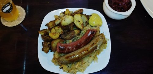 A plate of sausages, sauerkraut, roasted potatoes, and mustard, with a side of cranberry sauce.
