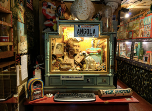 A quirky display featuring a bust, vintage items, and a sign reading "Angola Prison Rodeo" in a colorful museum setting.