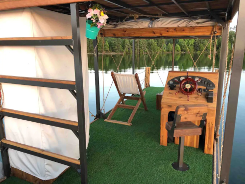 A cozy boat interior featuring a wooden steering console, a chair, and a view of calm water and greenery.
