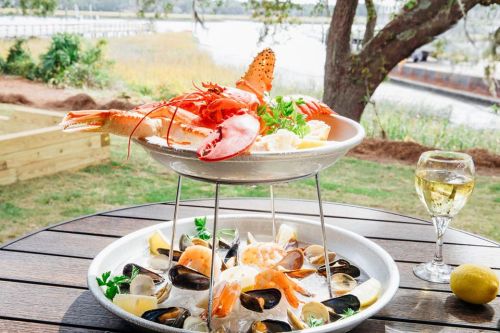 A seafood platter featuring lobster, shrimp, and shellfish, served with lemon and a glass of white wine outdoors.