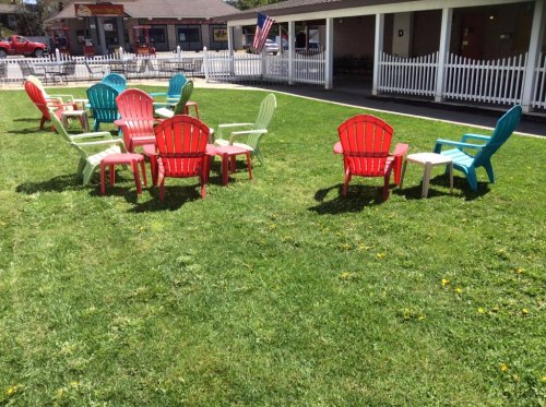 Colorful Adirondack chairs in red, green, and blue arranged on a grassy lawn with a white picket fence in the background.