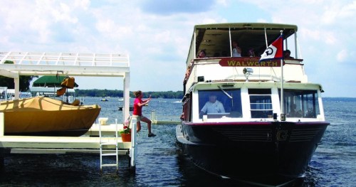 A boat approaches a dock with a person jumping onto the dock, while others relax on the boat.