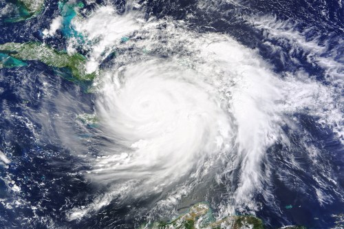 Satellite image of a large hurricane swirling over the ocean, with visible cloud formations and surrounding landmasses.