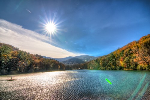 A serene lake surrounded by colorful autumn trees under a bright sun and clear blue sky.