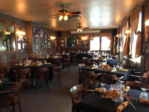 Cozy restaurant interior with wooden decor, tables set with black tablecloths, and warm lighting.
