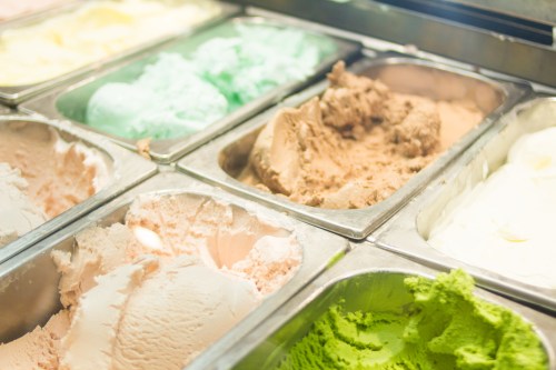 A variety of colorful ice cream flavors in metal tubs, including green, pink, brown, and white.