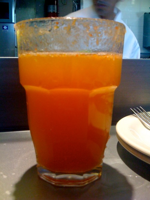 A tall glass filled with bright orange juice, sitting on a table with a blurred background.