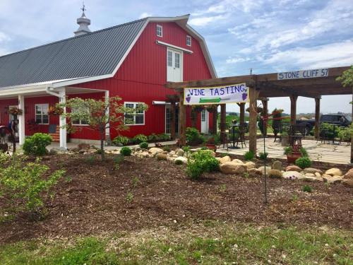 A red barn-style building with a patio area, featuring a "Vine Tasting" sign and landscaped gardens.