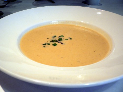 A creamy soup served in a white bowl, garnished with small green herbs on top.