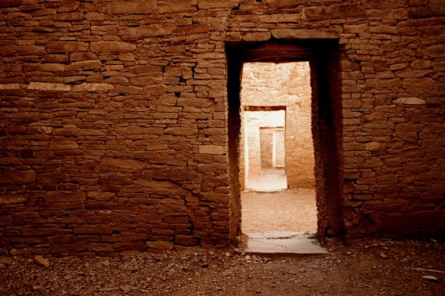 A doorway in a stone wall leads to a sunlit interior space, showcasing rustic textures and earthy tones.