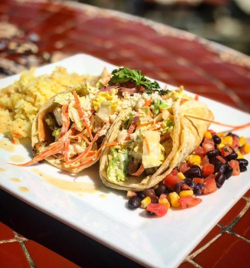 Two tacos filled with shrimp and vegetables, served with rice and a colorful side of black beans and corn salad.