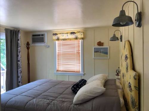 Cozy bedroom with a bed, window with blinds, wall art, and decorative lighting.