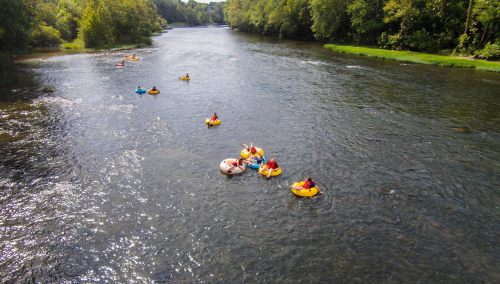 People floating on colorful inner tubes down a calm river, surrounded by lush green trees.