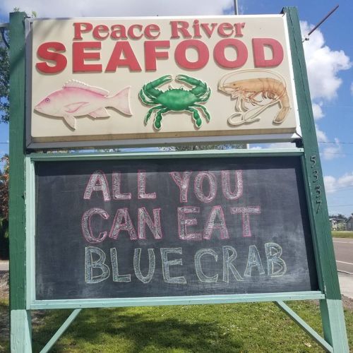 Sign for Peace River Seafood featuring seafood illustrations and a chalkboard announcement for "All You Can Eat Blue Crab."