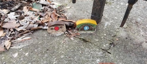 Two small wooden pieces with painted designs, resting on a concrete surface surrounded by dried leaves.