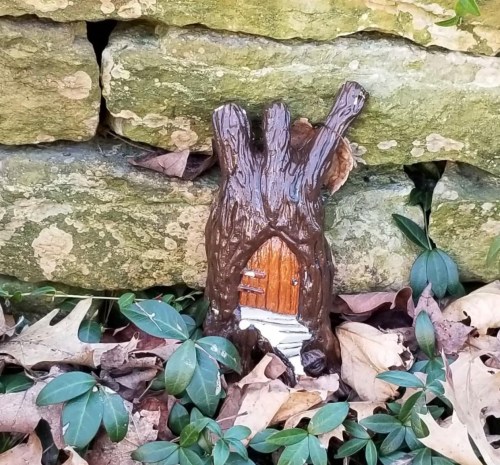 A small, whimsical tree stump with a door, nestled among stones and fallen leaves.