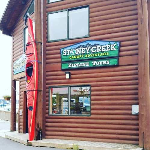 A wooden building with a sign for Stoney Creek Canopy Adventures and a red kayak displayed outside.