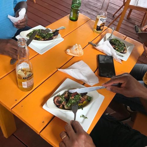 A vibrant orange table with plates of food, drinks, and hands holding utensils, enjoying a meal together.