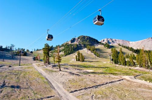 A scenic view of a ski resort with gondolas, mountains, and trees under a clear blue sky.