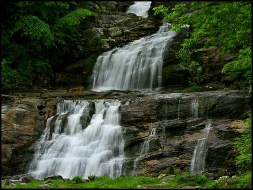 A serene waterfall cascading over rocky terrain, surrounded by lush green foliage.